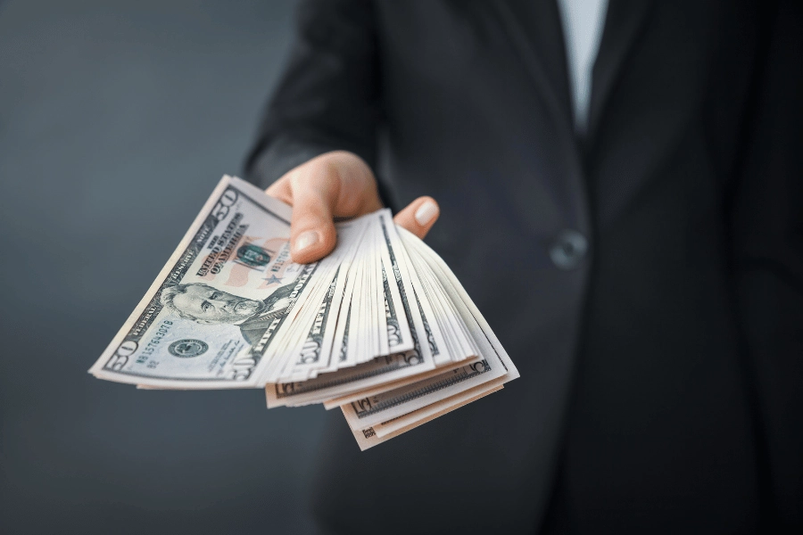 person in a black suit holding stack of cash 